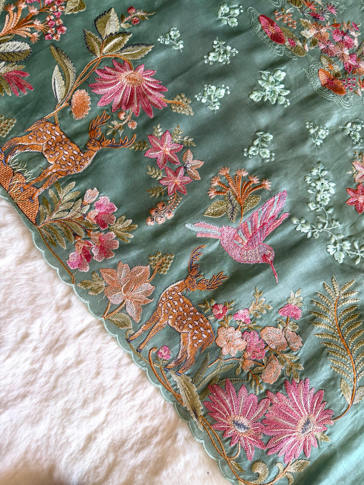 Embroidered fabric with floral and deer patterns on a green background