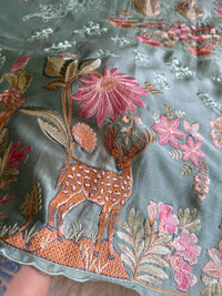 Embroidered fabric with a deer and floral design on a green background