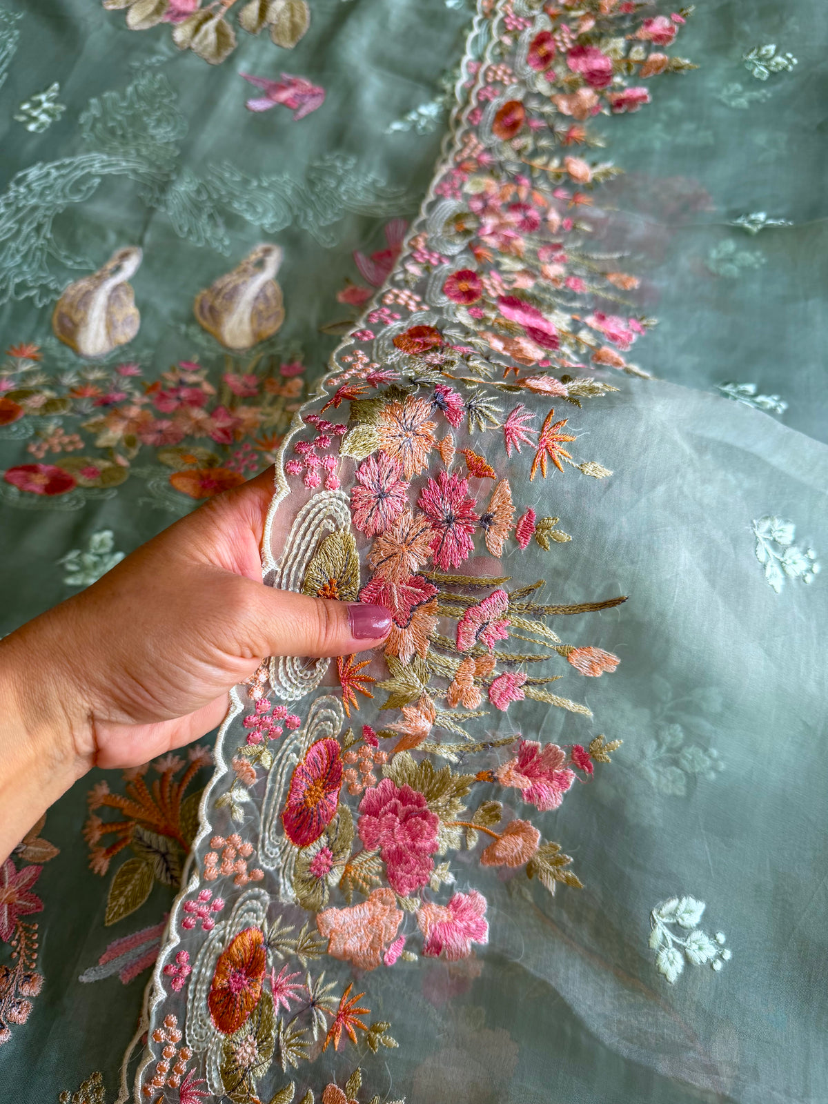 Close up of floral embroidery on fabric with a hand holding the edge of Dupatta.